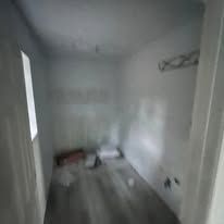 Empty unfinished room with white walls, gray floor, and tools/materials on the floor near a window.