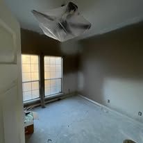 Empty room with two windows, bare carpet, and damaged ceiling in the corner.