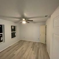 Empty bedroom with light wood floors, white walls, ceiling fan, and two windows.