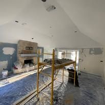 Renovation room with drywall patches, blue floor covering, scaffold, and paint supplies