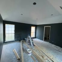 Renovated room with dark walls, white ceiling, windows, ladder, paint bucket, and floorboards being installed