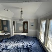 Bedroom with white walls, French doors, and a rumpled blue comforter on the bed.