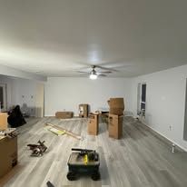 Living room with unpacked moving boxes, tools, and flooring materials, ceiling fan overhead