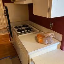 Narrow kitchen counter with gas stove, white cabinets, and a loaf of bread on the counter