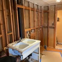 Bathroom under renovation with exposed studs, a sink on a stand, and doorways in the background