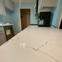 Narrow kitchen with teal walls and a white countertop; coffee maker and appliances along the sides.