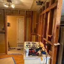 Partially stripped room with exposed studs, tools, and a stove, suggesting ongoing renovation.