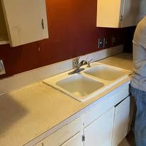 Kitchen sink and countertop with white cabinets and a person standing at the right edge.