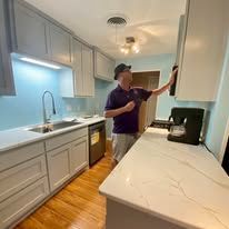 Man inspecting a bright white kitchen cabinet beside a marble countertop and sink