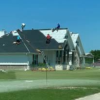Workers on a house roof after storm damage, with a fire hose spraying water in the foreground.