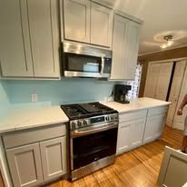 Modern kitchen with gray cabinets, white countertops, stainless-steel stove and microwave, and light wood floor
