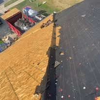 Roof with black shingles and exposed plywood underlayment during repair work.