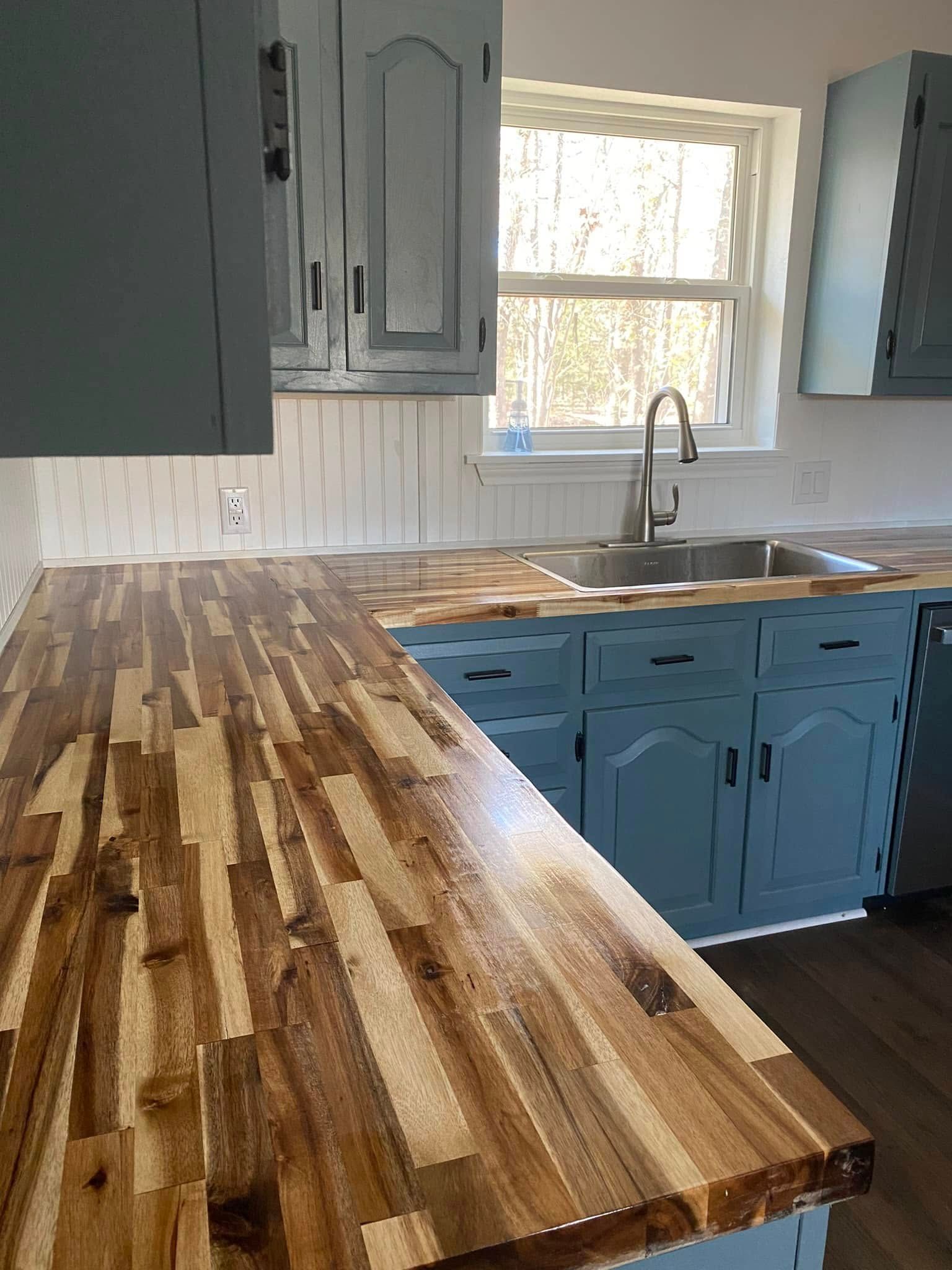Blue kitchen with butcher-block countertop, sink by window, and gray cabinets