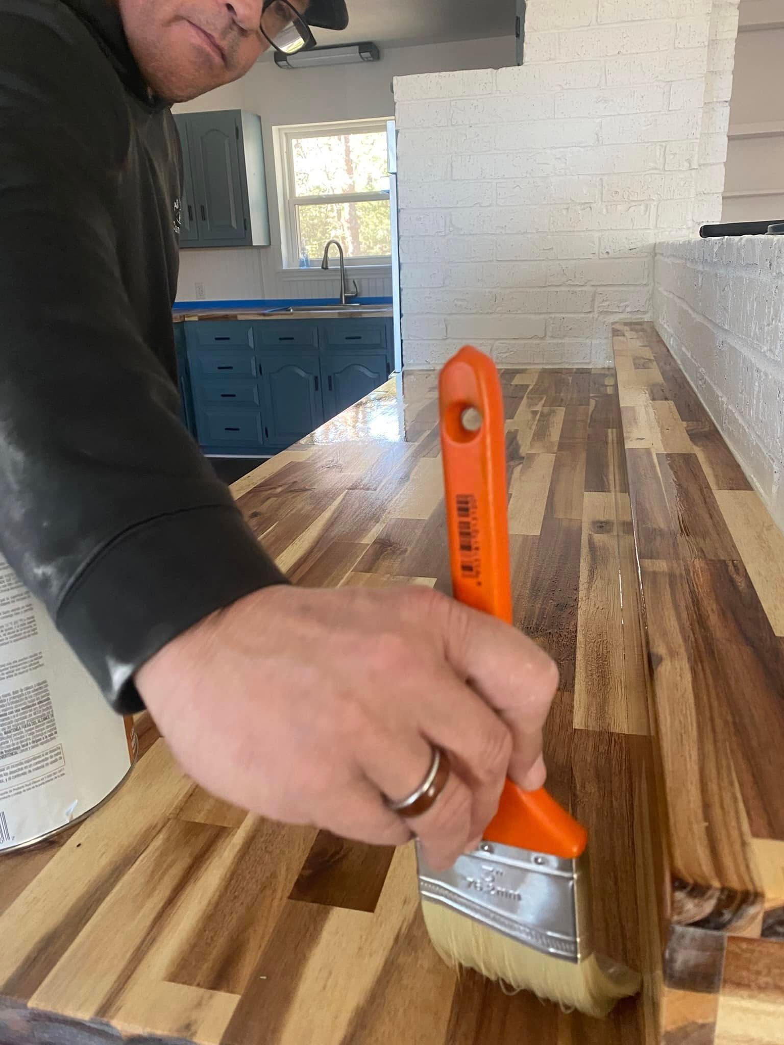 Person painting a striped wooden surface with an orange brush in a kitchen.
