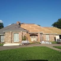 Single-story brick house with a tan roof and front lawn under a clear blue sky