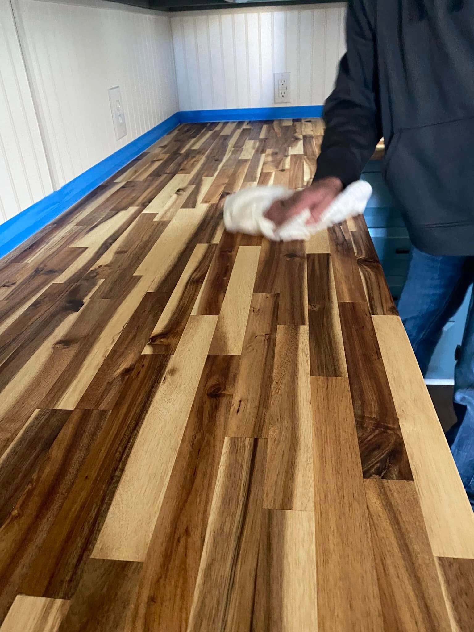 Person wiping a long wooden tabletop in a workshop with a cloth