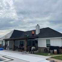 Workers on a house roof during repairs, with one person on the roof and another below under cloudy skies