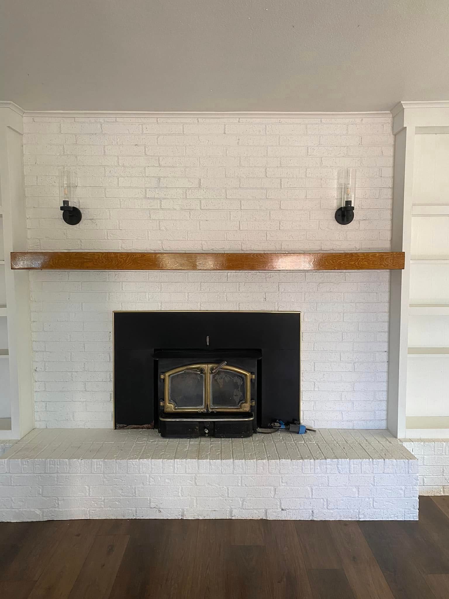 White brick fireplace with brass doors, wooden mantel, and dark hardwood floor in a living room