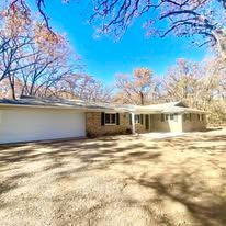 Single-story house with a white garage, stone facade, and leafless trees under a bright blue sky.