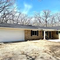 Single-story brick house with a two-car garage and bare trees in the yard on a sunny day