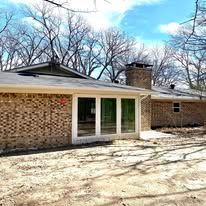 Single-story brick house with large glass doors and a chimney, seen in a leafless yard under a blue sky