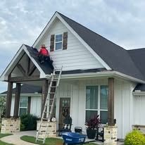 Worker on ladder repairing roof of white house with dark shingles