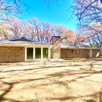 Brick house with a covered patio and leafless trees under a bright blue sky