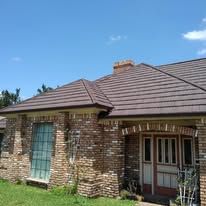 Brick house exterior with brown tiled roof, front door, and large window under a blue sky