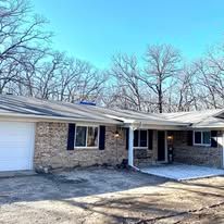 Single-story stone house with a white garage door, covered porch, and leafless trees in front