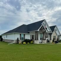 Modern single-story white house with dark roof and front porch on a large green lawn under cloudy sky