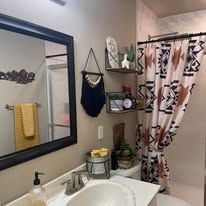 Small bathroom with sink, mirror, shelves, shower curtain, and yellow towel.