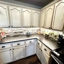 Bright kitchen corner with cream cabinets, dark countertops, stone backsplash, and hardwood floors