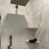 Tiled shower corner with wall shelves, a showerhead, and a black towel on one shelf.