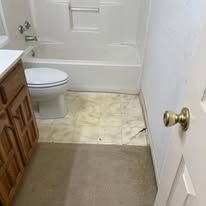 Small bathroom with toilet, tub, beige floor, and a white door with brass knob open in foreground