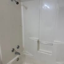 White bathtub and shower surround with chrome faucet and knobs in a bathroom.