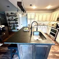 Kitchen interior with dark island, farmhouse sink, white cabinets, and open shelving.