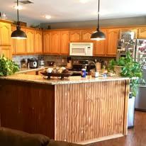Warm kitchen with wooden cabinets, central island, pendant lights, and potted plants by the sink.
