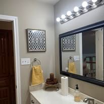 Bathroom vanity with mirror, lights, and white sink countertop; towel and soap dispensers nearby