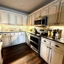 Bright cream kitchen with dark wood floor, stainless steel stove and microwave, and under-cabinet lighting