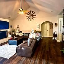 Spacious living room with dark wood floors, sectional sofa, TV, ceiling fan, and decorative wall clock