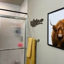 Bathroom with frosted shower door, yellow towel, and framed highland cow wall art