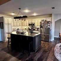Modern kitchen with dark island, stainless steel appliances, cream cabinets, and hardwood floors.