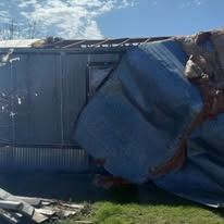 Collapsed blue metal shed with bent walls and a torn roof in a grassy outdoor area