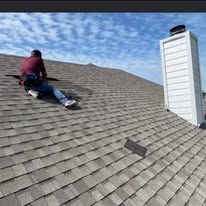 Person kneeling on a shingled roof beside a chimney, inspecting roof damage