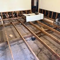 Exposed floor joists in a room under renovation with a white sink basin in the center