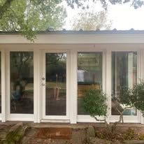 Modern white house exterior with tall glass doors and surrounding trees and shrubs