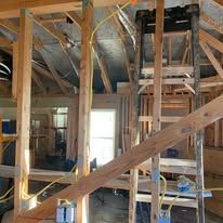 Unfinished house interior with exposed framing, insulation, and a ladder on a loft platform.