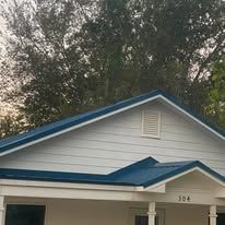 White house facade with blue roof trim and a front porch, partly obscured by trees