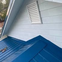Blue metal roof beneath light gray siding with a white louvered vent.