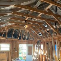 Interior of a house under renovation, with exposed wooden roof trusses and unfinished framing.